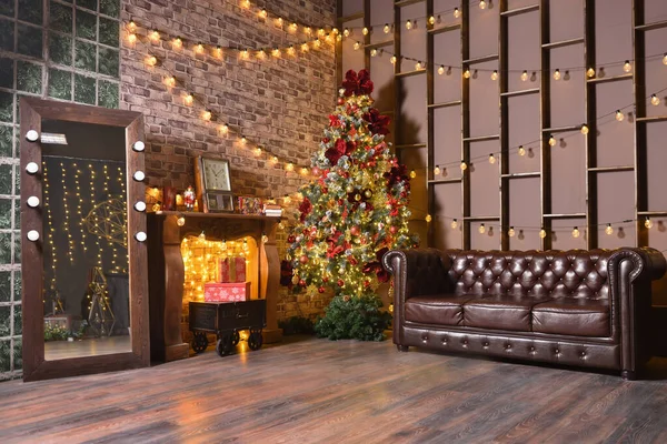 Snygg jul loft dekorationer i ett brunt vardagsrum med en skinnsoffa, julgran och girlanger med glödlampor på väggen — Stockfoto