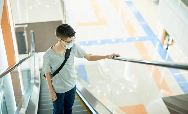 12-jähriger Junge trägt Gesichtsmaske auf Rolltreppe in Einkaufszentrum Stockfoto