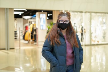 Alışveriş merkezinde siyah maske takan genç bir kadının portresi.