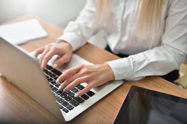 Kadın eller ofisteki dizüstü bilgisayarın klavyesinde yazı yazıyorlar.