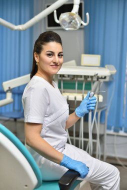 Sandalyede oturan ve elinde diş aletleri olan genç bir dişçinin portresi.