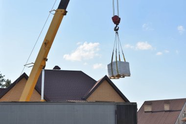 Kamyon vinci, özel bir evin arka planında inşaat malzemeleri taşıyor.