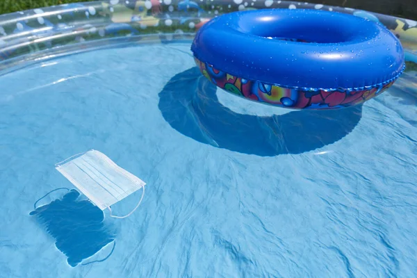 Máscara protectora flota en una piscina inflable para niños, el concepto de unas vacaciones junto al mar y la pandemia de coronavirus — Foto de Stock