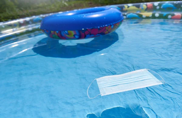 Máscara protetora em uma piscina inflável infantil, o conceito de férias à beira-mar e a pandemia de coronavírus — Fotografia de Stock