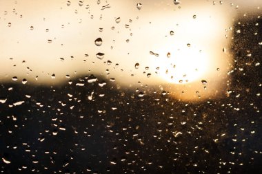 Pencere camında yağmur damlaları, gün batımı, şehirde akşam