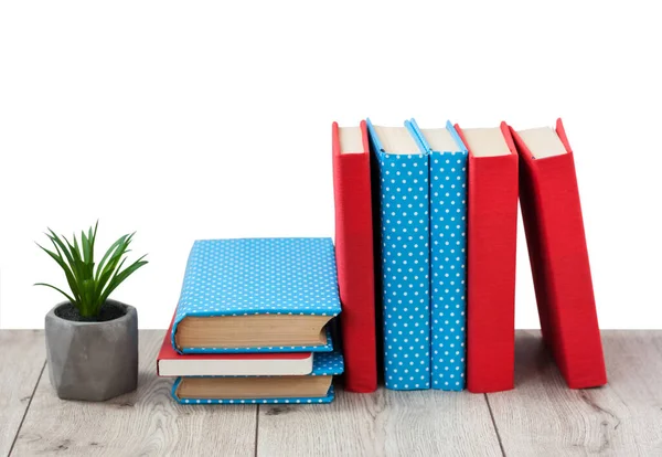 Renkli kapaklarda kitap yığını ve beyaz arka plandaki tahta masada saksıya bitki. Okul mesafesindeki ev eğitimine geri dönüyoruz. Evde kalma karantina kavramı.