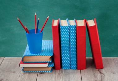 Renkli kapaklarda kitap yığını ve ahşap masa üzerinde yeşil karatahta arka planı olan kalemler. Uzaktan eğitim. Okula dönmek, karantina konsepti evde kalmak.