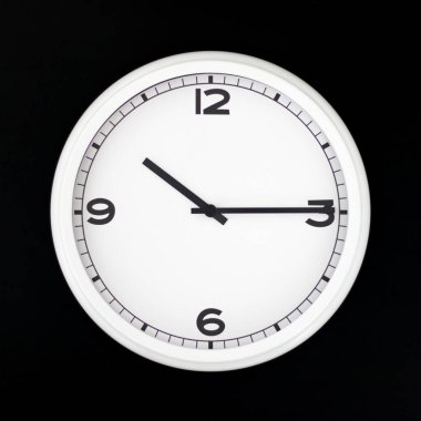 Beyaz yuvarlak analog duvar saati siyah arkaplanda izole edilmiş, saat onu çeyrek geçiyor..