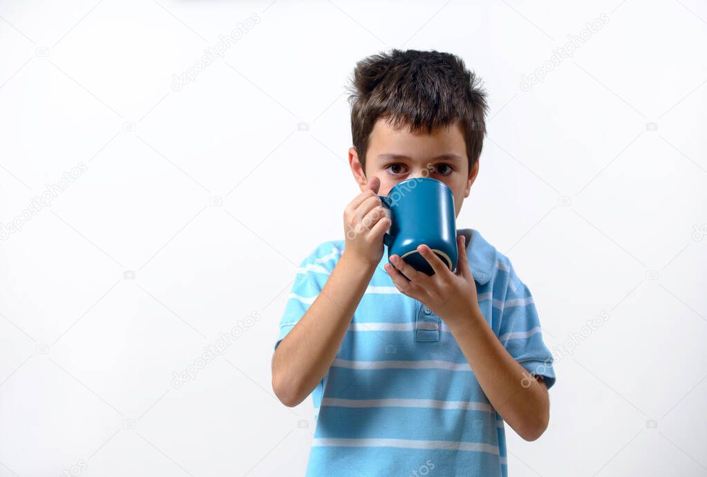 The boy in a blue T-shirt drinks from a blue cup on a light background.