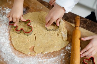 Çocuklar hamurdan kurabiye kestiler. Erkek kardeşi ve kız kardeşi evde kurabiye pişirir. Eller yakın plan..