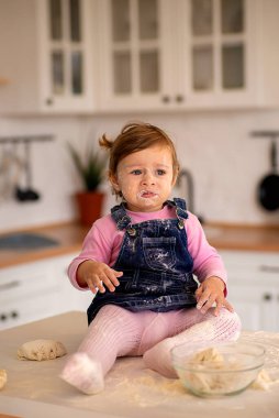 Kız masada oturuyor, yüzü ve kıyafetleri un içinde.