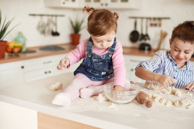 Küçük kız elini un dolu bir tabağa koydu, arka plandaki oğlan hamuru yoğurdu.