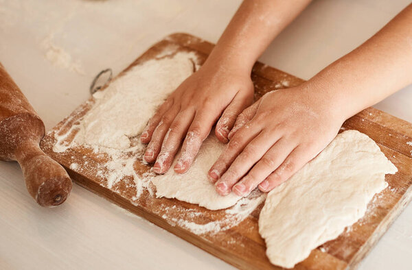 Children's hands lie on top of the dough rolled on a wooden board