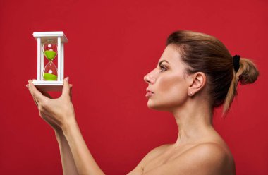 Kırmızı arka planda elinde kum saati olan profildeki genç kadın..