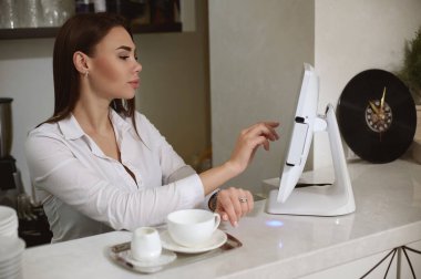 Beyaz üniformalı genç bir barista monitörde parmak izi siparişi veriyor.