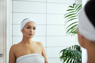 Banyodaki aynada yansımasına bakan genç kadın.