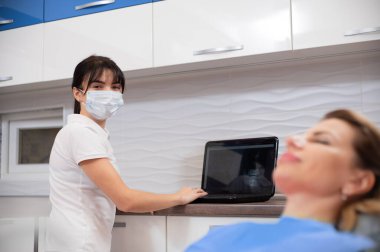 Diş hekimliği ofisinde tıbbi maske takmış bir dişçinin portresi.