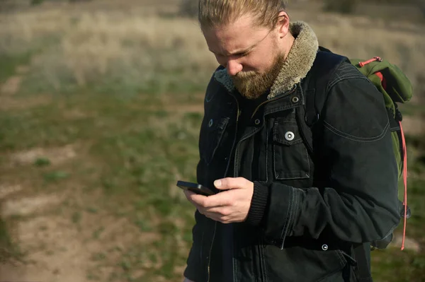 Portrait of an adventurer man using smartphone while hiking, searching signal, or looking for direction.