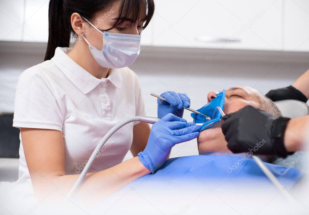 Female dentist wearing a ptotective medical mask treating a patient on a dental office.