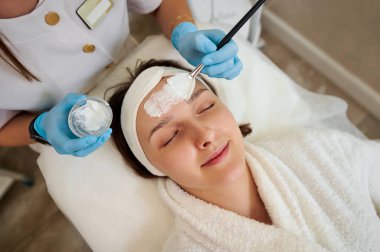 Kozmetik uzmanı güzel genç bir kadının yüzüne doğal bir maske takıyor..