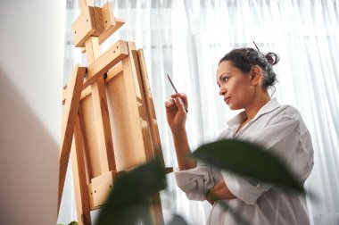 Güzel kadın ressam atölyede sehpanın önünde duruyor.