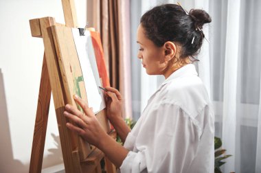 Sanatçı veya tasarımcı kadın kalem kullanarak resim çiziyor ve resim sehpasının önünde duruyor.