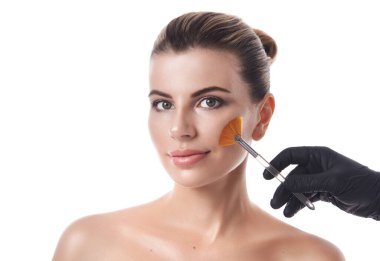 Güzel bir genç kadının beyaz arka planında izole edilmiş bir portre ve yüzüne yakın fırçayı tutan siyah eldivenli bir el..