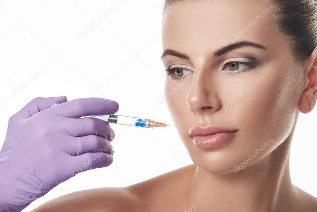 Beautician's hand in purple glove holding a syringe near beautiful woman's face. Portrait isolated on a white background.