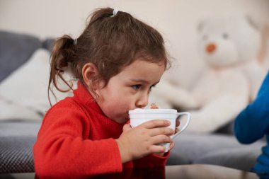 Kırmızı kazak giyen güzel bir kız çocuğu lokumlu lezzetli bir kakao içiyor..