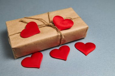 Sevgililer Günü 'nün hediye kutusu el işi kağıdına sarılı ve kırmızı kalpler gri arka planda.