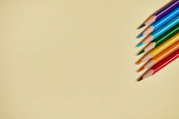 Colored pencils form the colors of rainbow on a yellow background. Flat lay, copy space, top view. Office