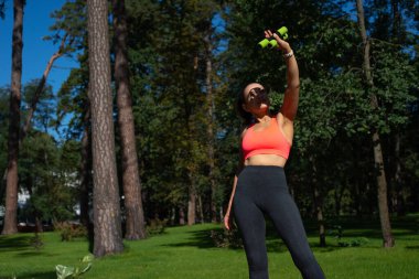 Küçük dambıllar tutan genç, sportif bir kadın ve kaldırılmış kollara bakıyor.