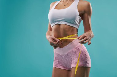 Güzel, formda bir kadının karın ölçüsü bant kullanarak beklemesini ölçen vücudu ve düz karnı. Mavi bir arkaplanda izole edilmiş