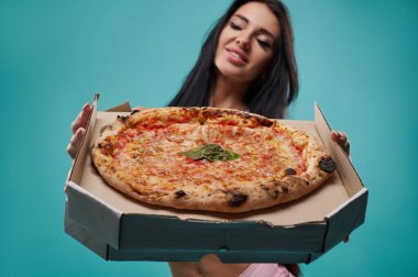 Neşeli genç, zayıf bir kadın elinde lezzetli taze pizzayla bir kutu tutuyor ve kameraya gösteriyor. Pizzaya odaklan..