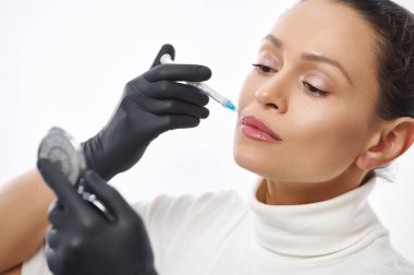 Çekici bir kadının beyaz bir arka planda izole edilmiş yan güzellik portresi aynaya bakıyor ve dudaklarına iğne yapıyor.