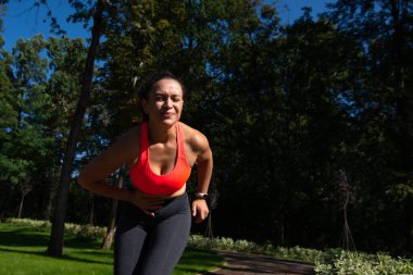 Dışarıda egzersiz yaparken yan tarafına kramp giren bir kadın. Koştuktan sonra karın ağrısı. Spor sakatlığı