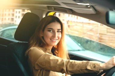 Gülümseyen genç bir kadın güneşli bir günde araba sürmekten zevk alıyor.