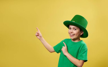 İrlanda cüce şapkalı komik bir çocuk. Parmağıyla kameraya bakıyor ve sarı arka planda fotokopi çekiyordu..