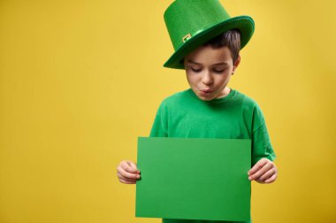 Yeşil cüce şapkalı küçük çocuk elindeki yeşil kağıt parçasına bakıyor. Uzayı kopyala Aziz Patrick Günü konsepti