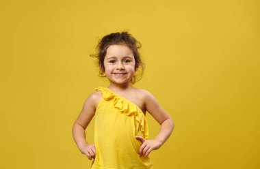 Güzel küçük kız kameraya poz veriyor. Sarı arka planda fotokopi çekiliyor.