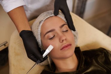 Güzellik uzmanı, güzellik salonunda yüz bakımı sırasında dinlenen beyaz saçlı güzel bir kadının yüzüne yakın bir fırça tutuyor..