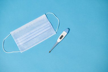Yüksek açılı koruyucu tıbbi maske ve mavi arkaplan termometresi