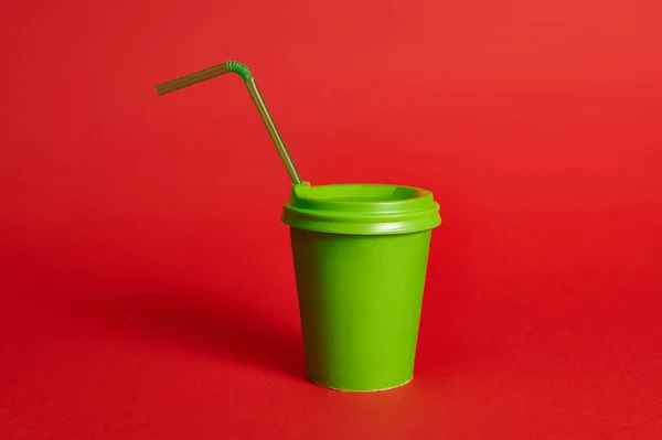 Studio shot of green recycled cardboard cup with straw on red background. Copy space. Shot with soft shadow. Color contrast