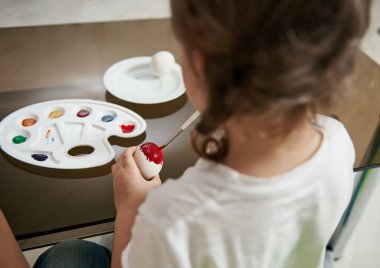 Paskalya yumurtasını süslemek için boya fırçası ve kırmızı boya kullanan tatlı bir kızın arka görüntüsü. Olay, Paskalya