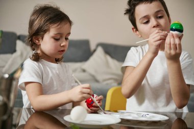 İki sevimli çocuk Paskalya yumurtalarını renkli boyalarla boyamaya odaklanmış..