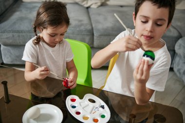İki sevimli çocuk Paskalya yumurtalarını renkli boyalarla boyamaya odaklanmış..