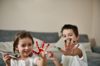 Kameraya renkli boya bulaşmış iki mutlu çocuk ellerini gösteriyor.