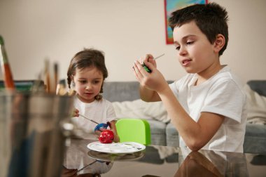 İki neşeli çocuk Paskalya için renkli yumurta hazırlıyor, onları renkli boyalarla süslüyor.