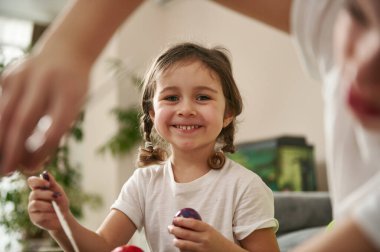 Paskalya yumurtasını süslerken kameraya bakan, dişlek gülüşlü, tatlı bir kızın ellerine bak..