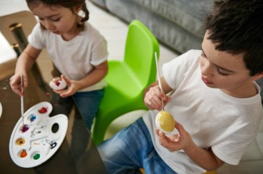 Paskalya yumurtalarını renkli boyalarla süsleyen iki sevimli çocuğun yüksek açılı görüntüsü. Geleneksel Paskalya kutlaması kavramı